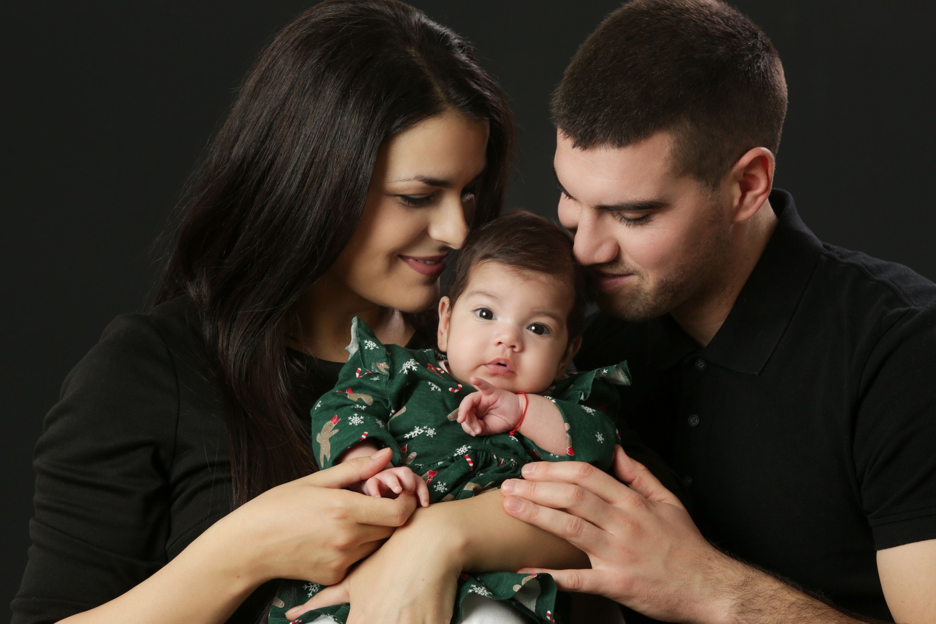 Studio portrait of young parents holding their little baby girl in green Christmas outfit, winter holiday, family memories, the first Christmas together